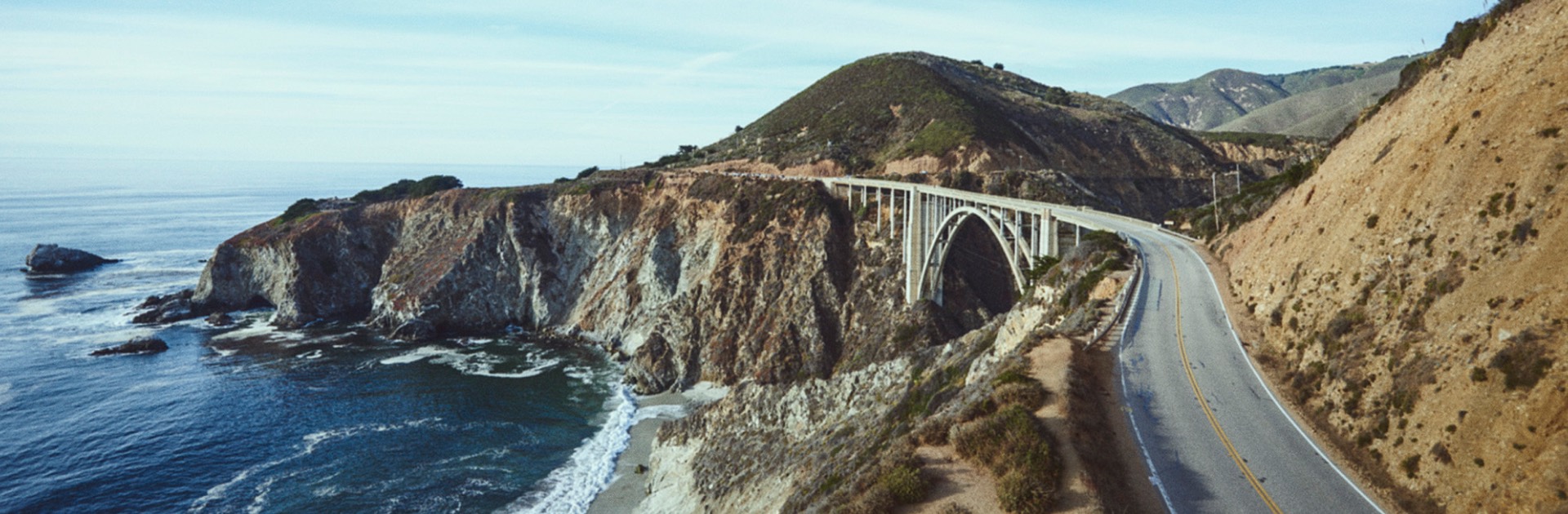 Coastal road crossing Bixby Creek Bridge with ocean and cliffs in the background.