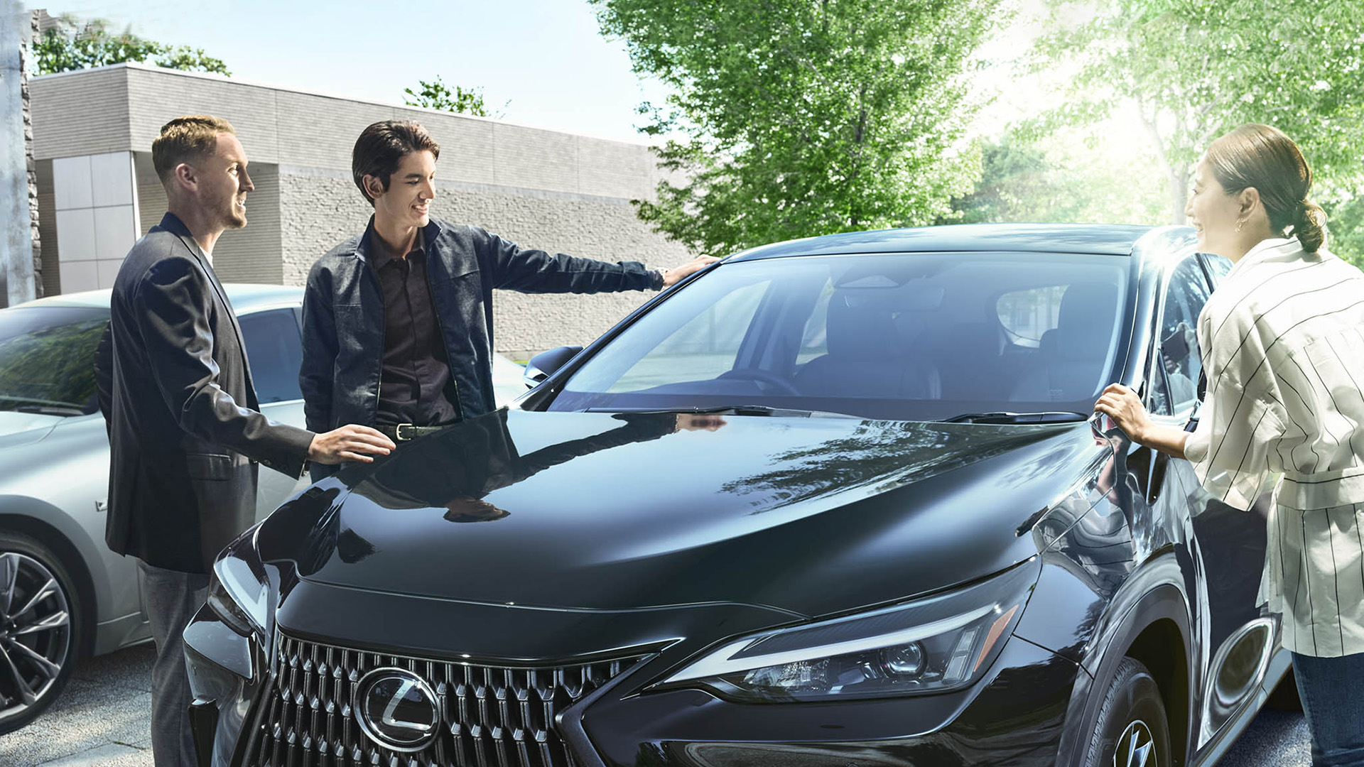 Three people gather around a black Lexus vehicle