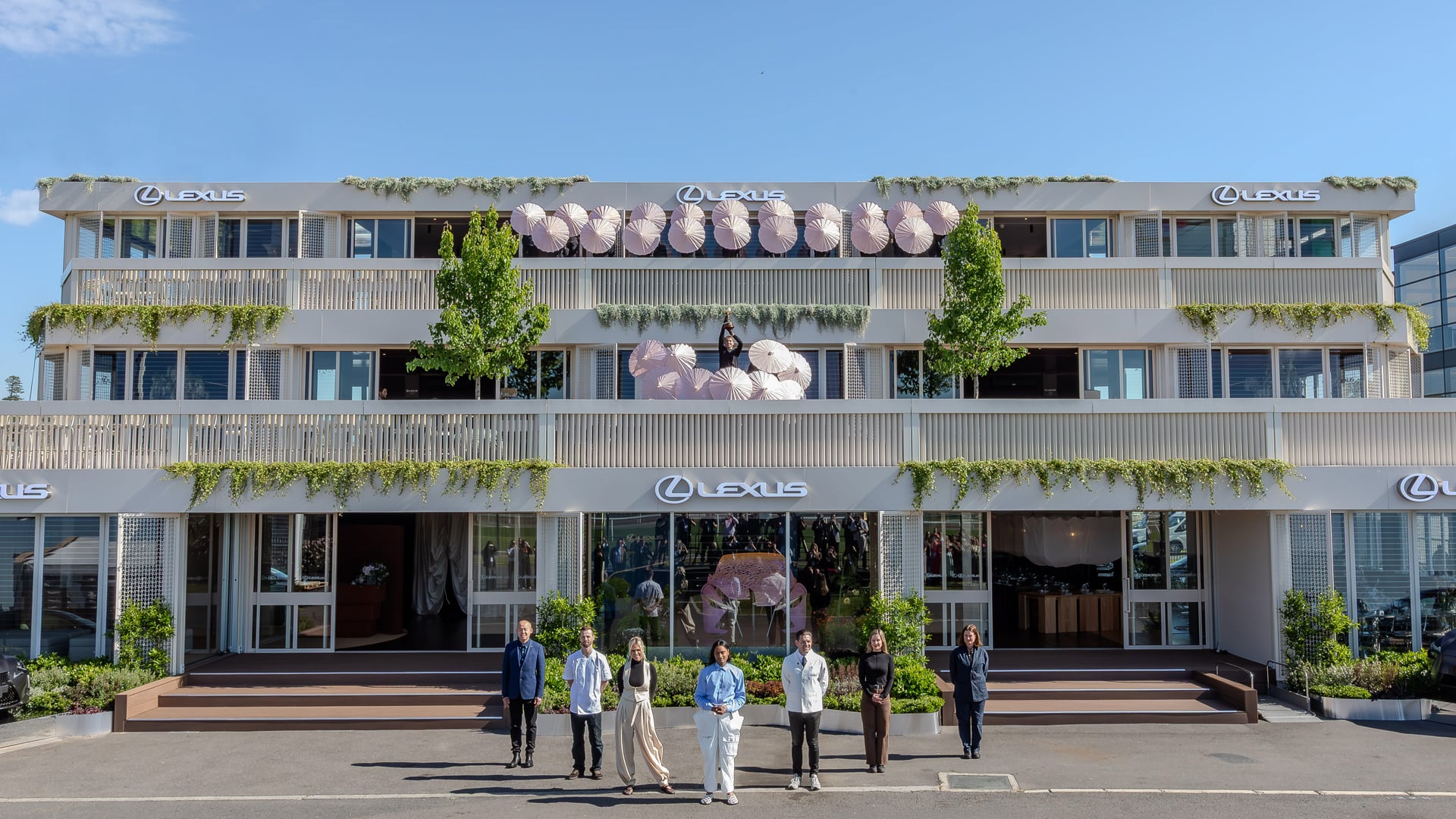 Three-level LANDMARK by Lexus pavilion with people standing in front and parasols displayed on the balconies