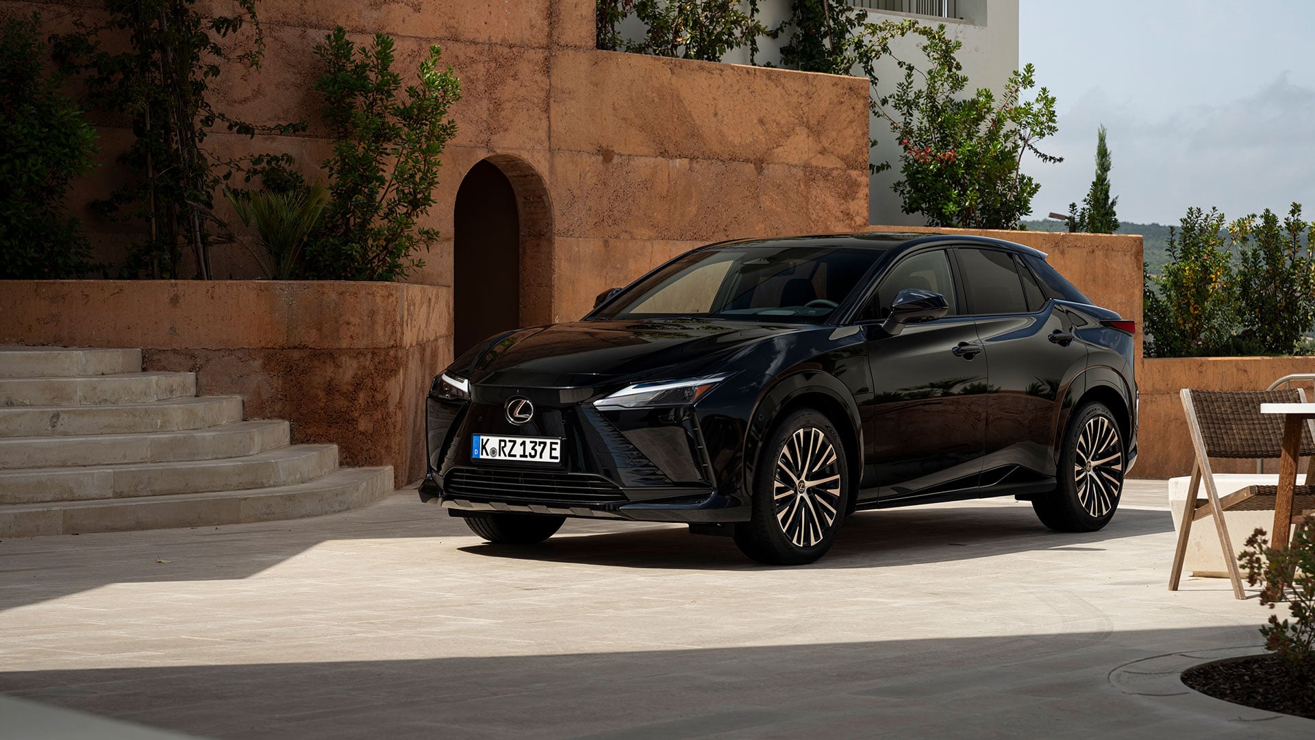 Black Lexus RZ electric SUV parked in a modern architectural courtyard with stone walls and greenery